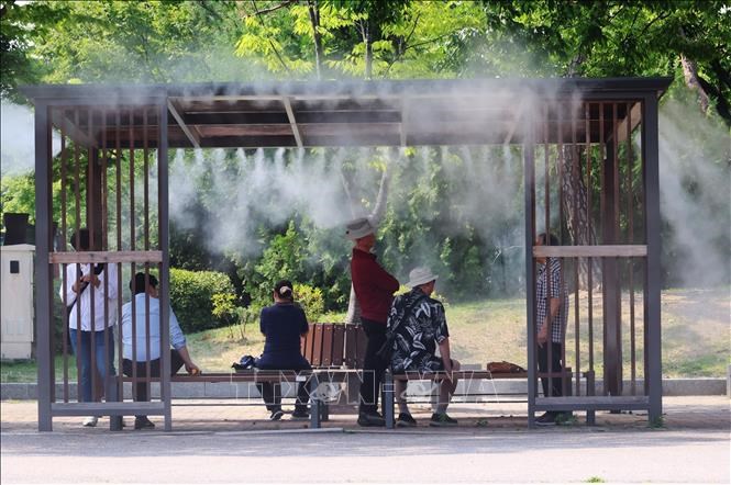 Người dân tránh nóng bên dưới hệ thống phun sương tại một công viên ở Seoul, Hàn Quốc. Ảnh: Yonhap/TTXVN